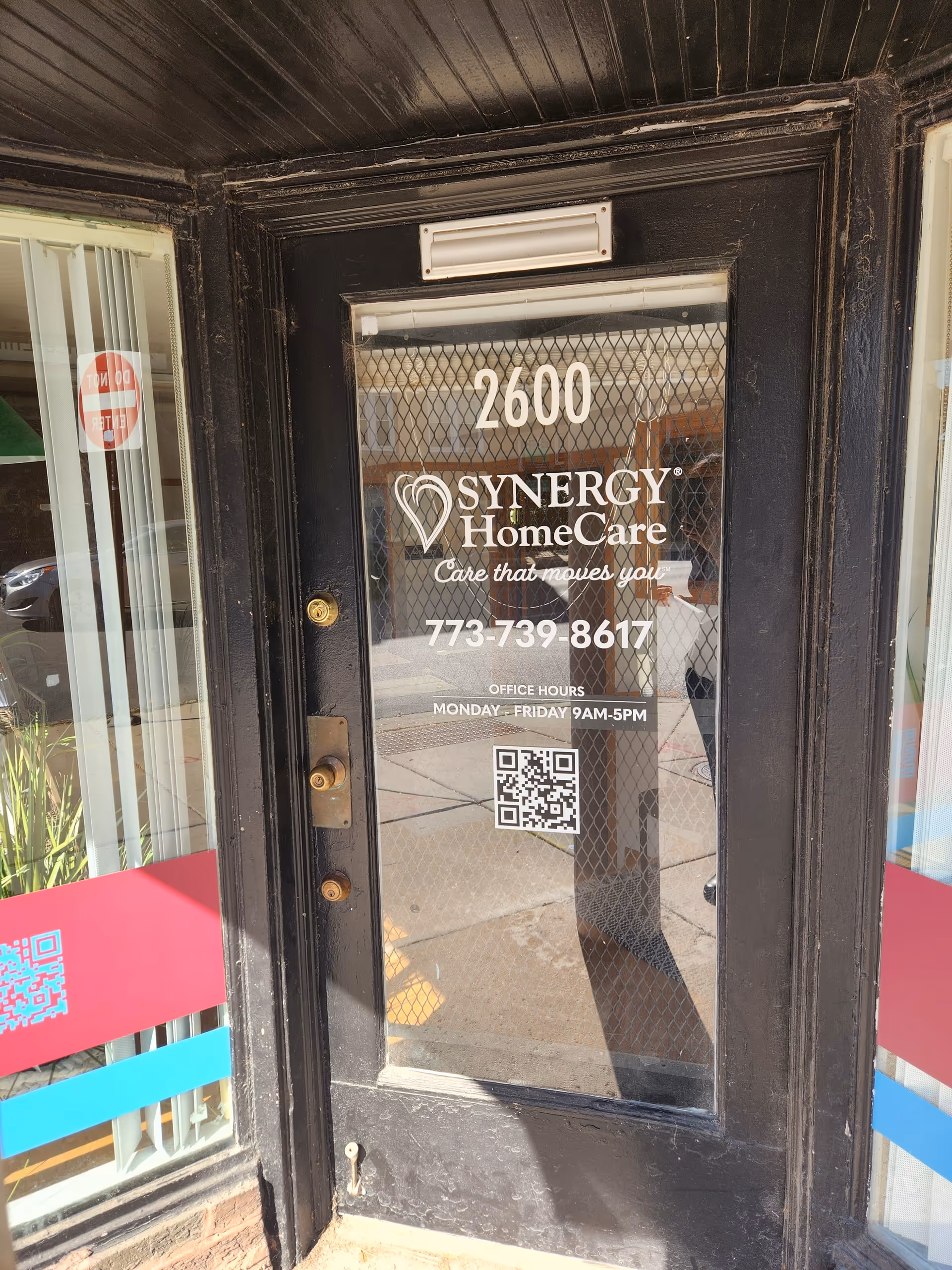 Black entrance door displaying Synergy HomeCare logo, address 2600, and phone number.