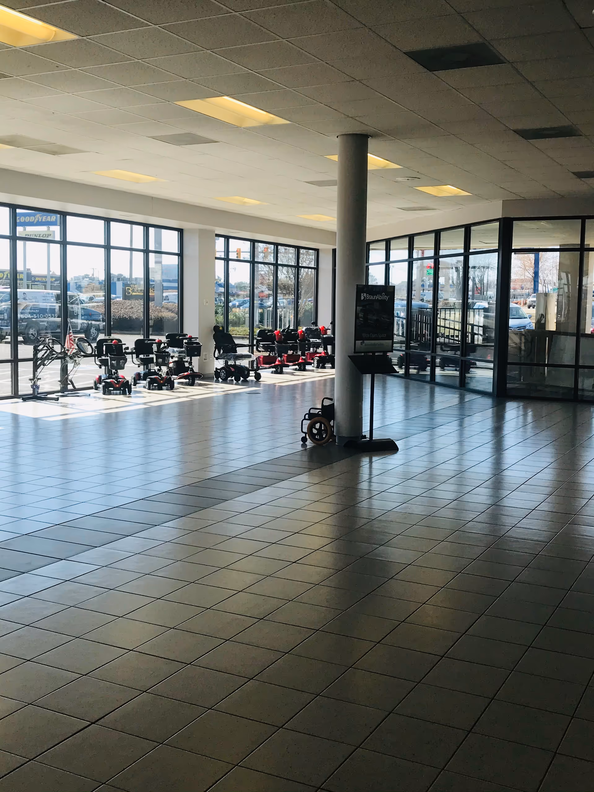 A spacious showroom with mobility scooters lined up along glass windows inside a lobby.