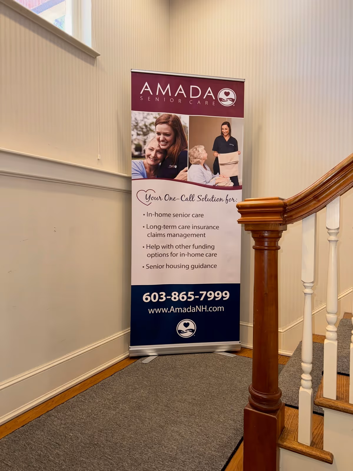 Indoor hallway with a vertical Amada Senior Care banner beside a wooden staircase.