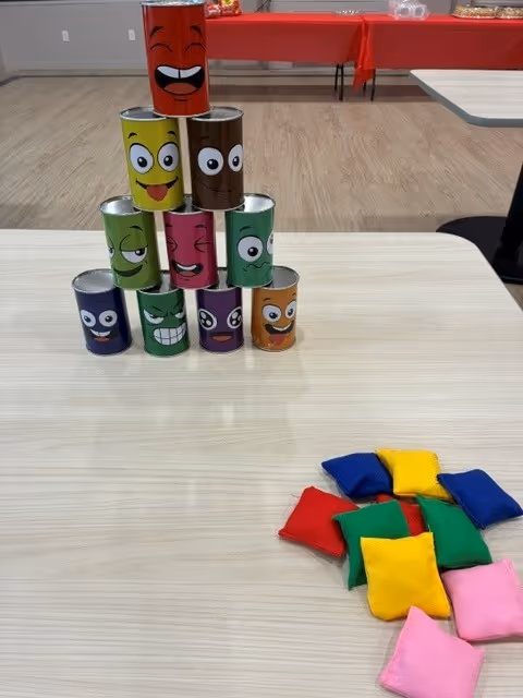 Stacked colorful cartoon cans on a table with scattered fabric cushions in a bright room