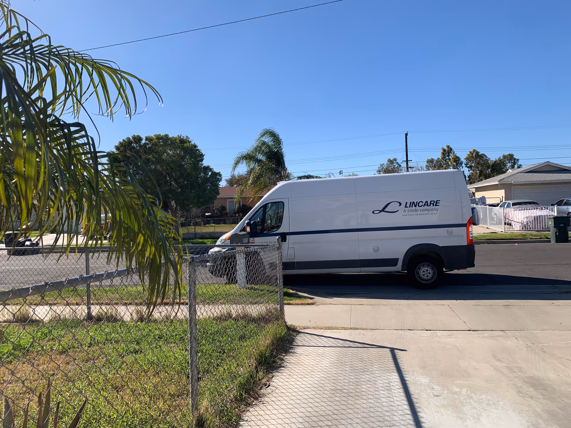 White LINCARE van parked on a residential street with a palm tree and chain-link fence.