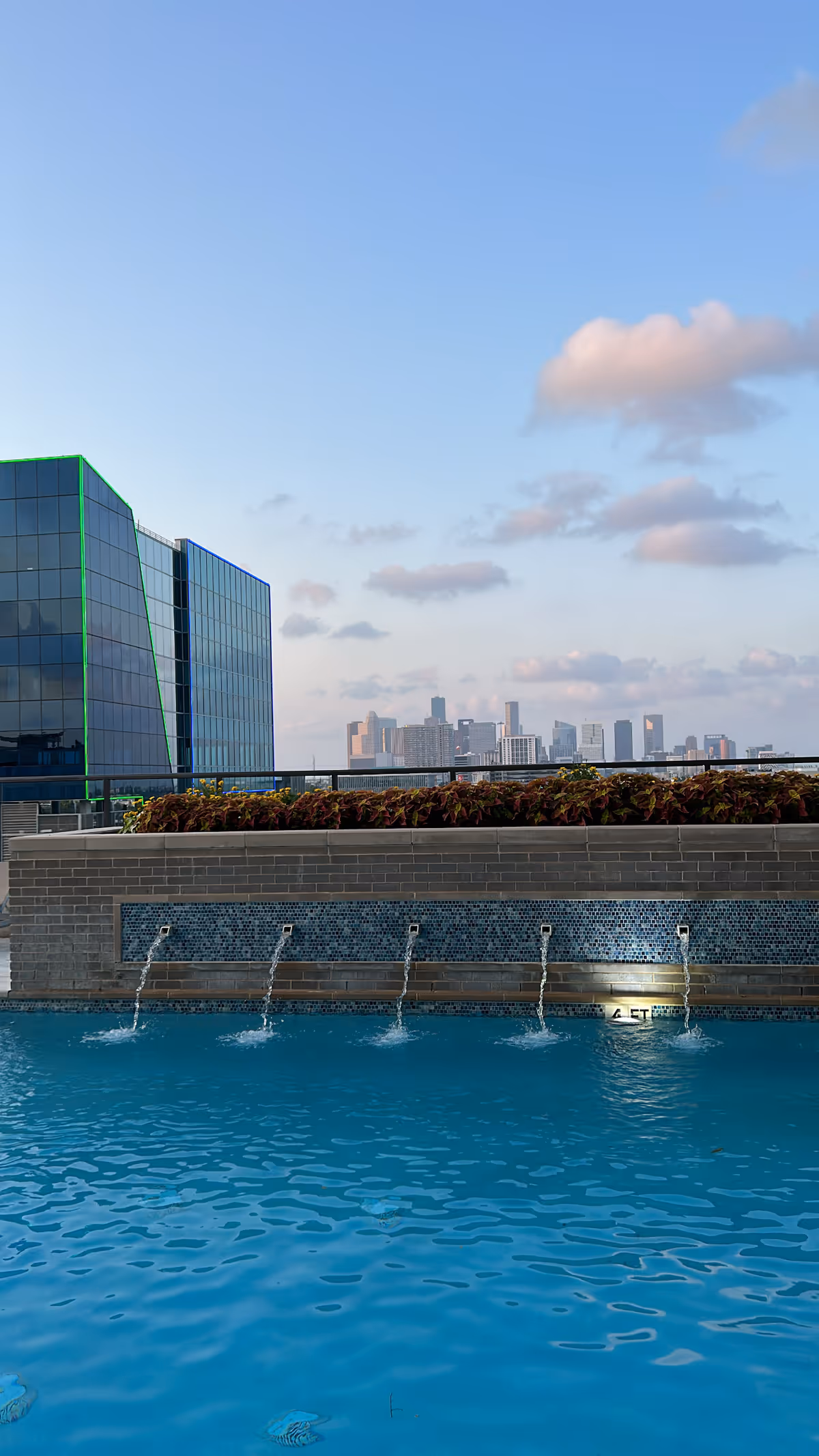 Outdoor pool with fountains and city skyline in view.