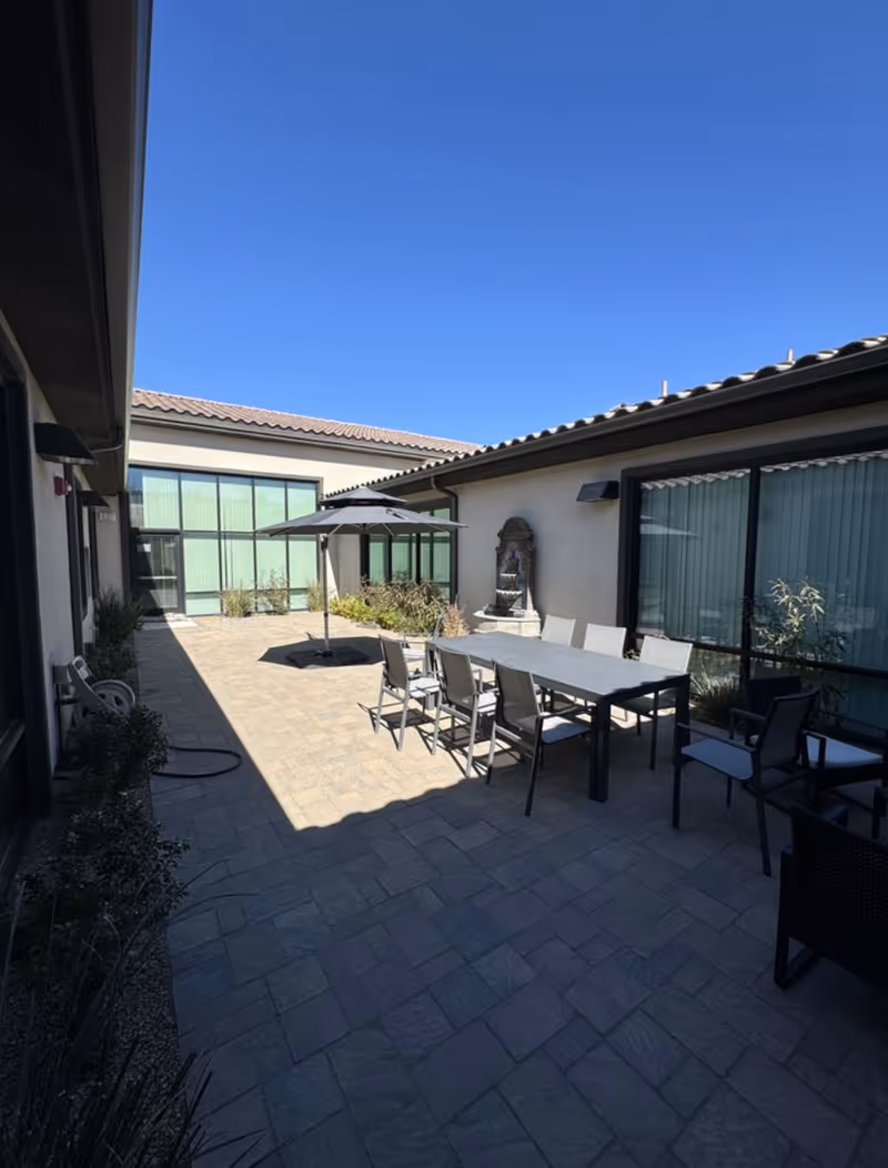 Outdoor courtyard with a long dining table, chairs, umbrella, and a fountain feature.