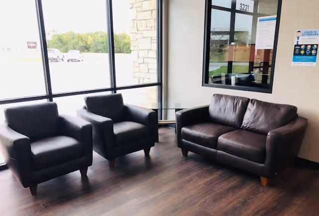 A modern interior waiting area with black leather chairs and a glass coffee table.