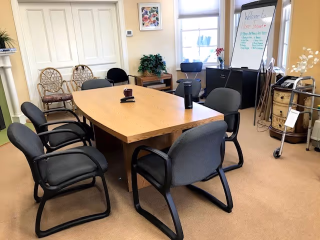 A wooden conference table with black chairs in a bright meeting room with a whiteboard.