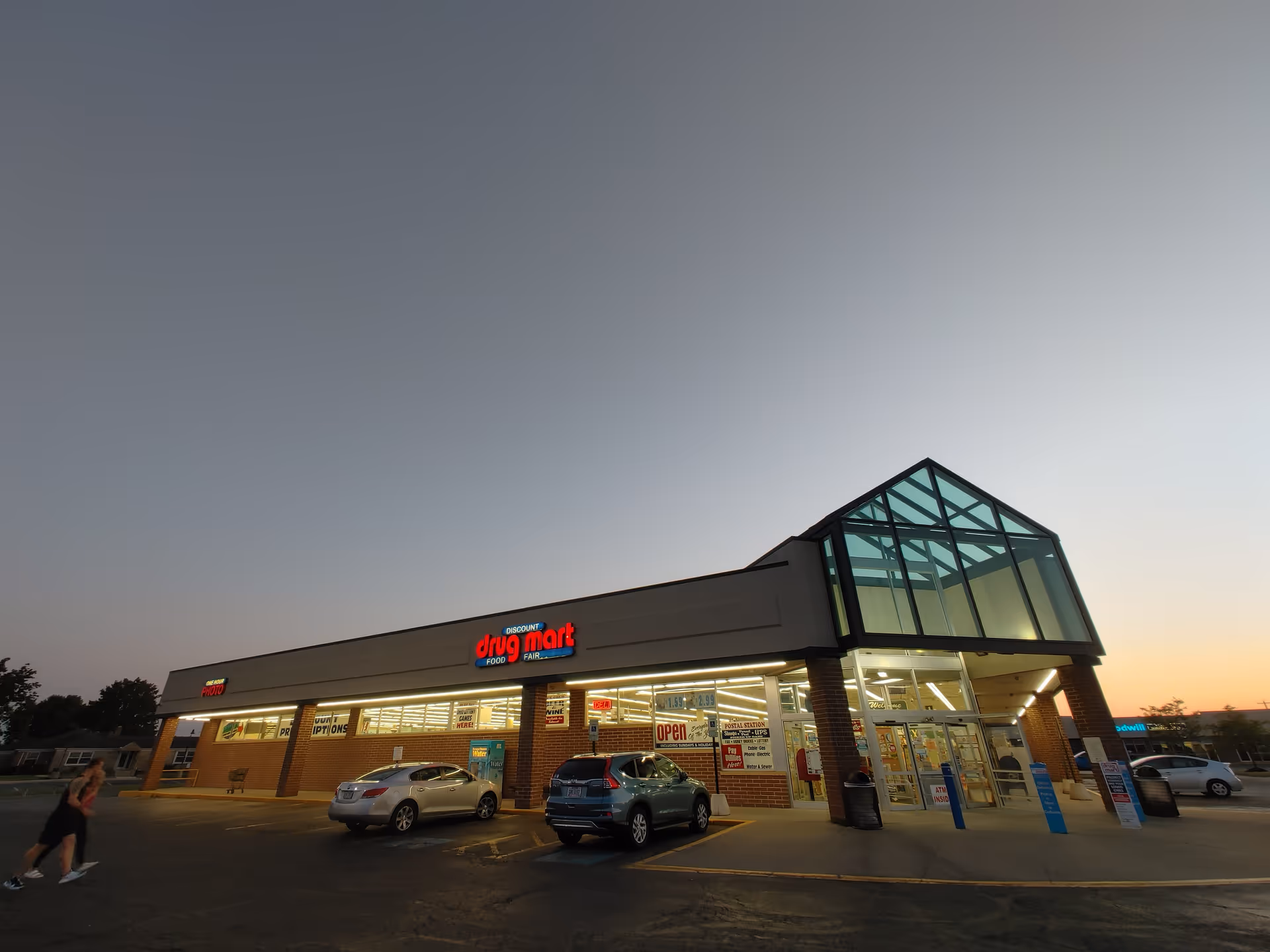 Exterior view of Discount Drug Mart storefront with glass entrance and parked cars.
