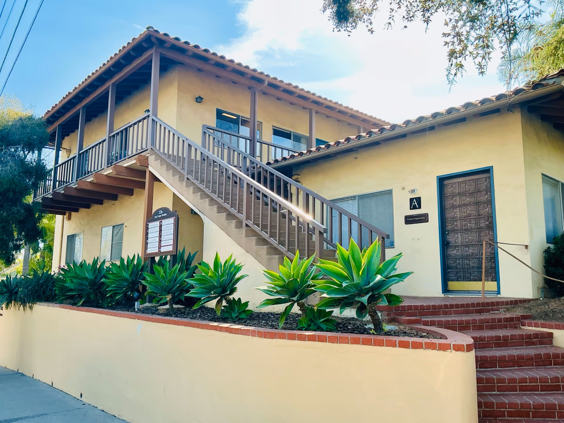 Two-story beige senior living building with exterior stairs and landscaping.