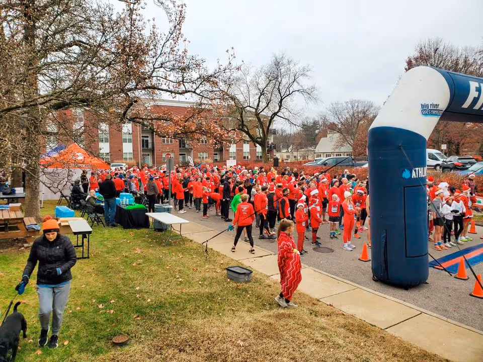 Large group of people in red gather for an outdoor charity run near a building.