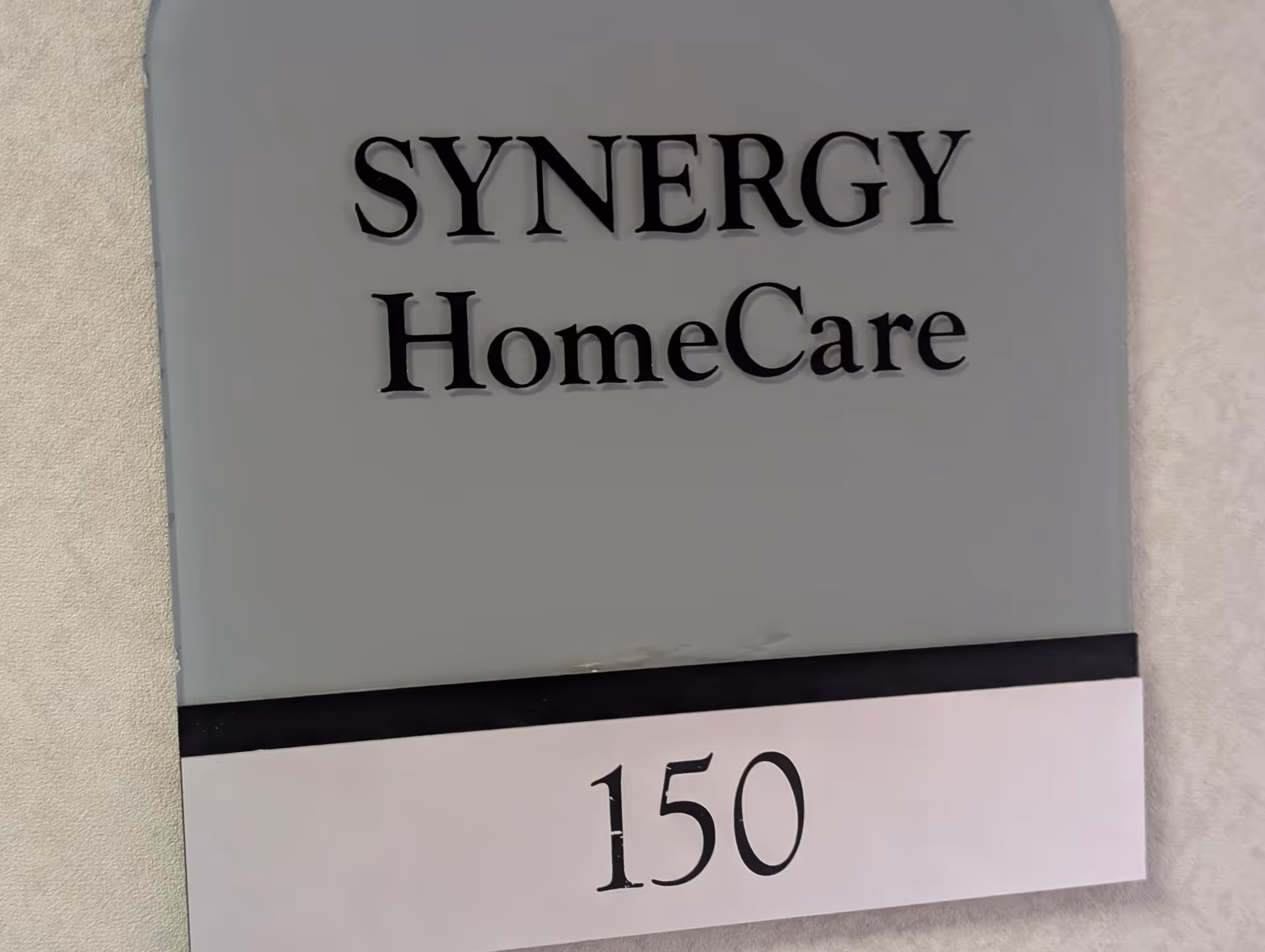 Grey SYNERGY HomeCare sign with 150 mounted on a wall