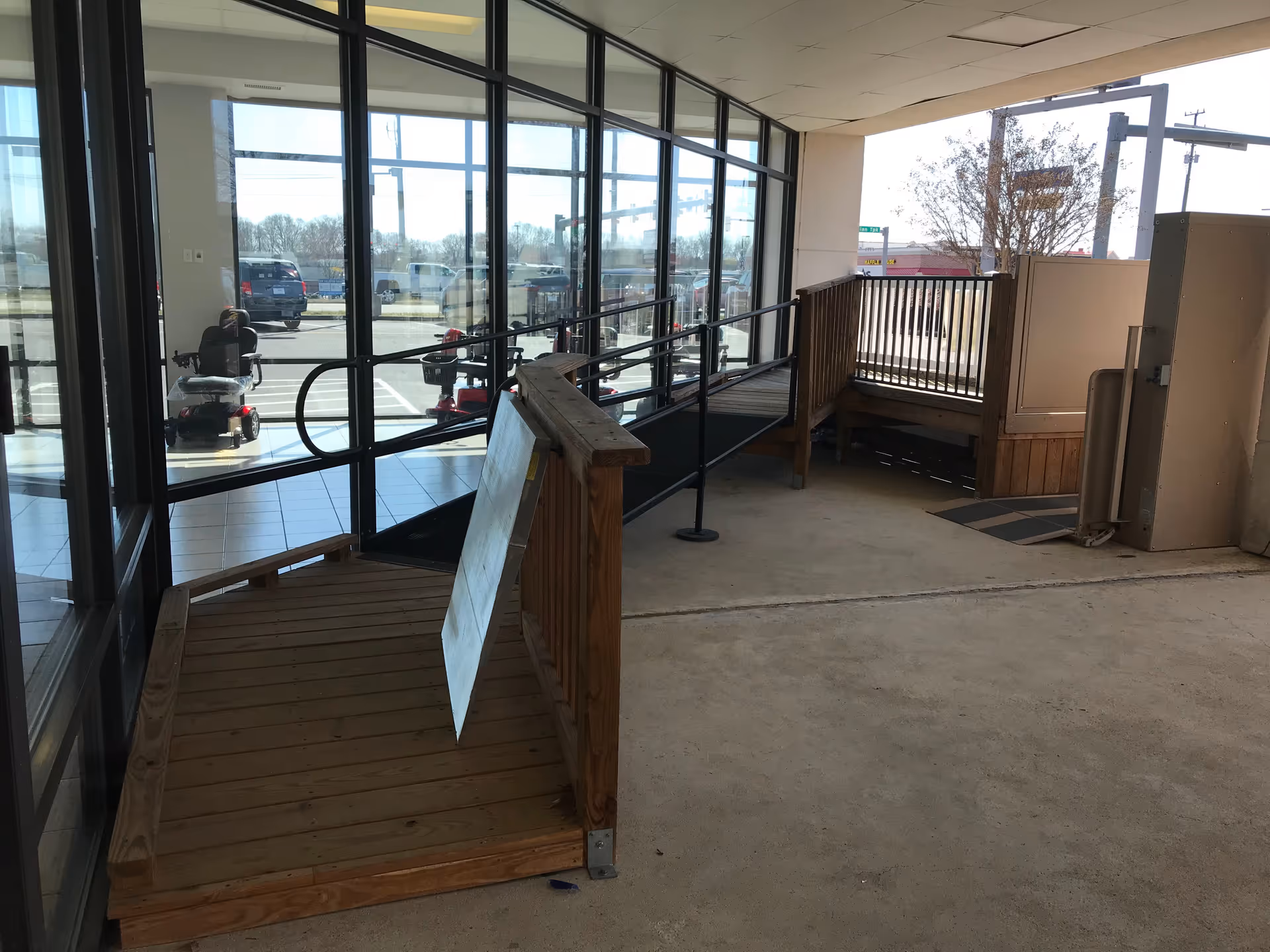 Glass-walled hallway leading to an outdoor wooden ramp and deck at a mobility facility