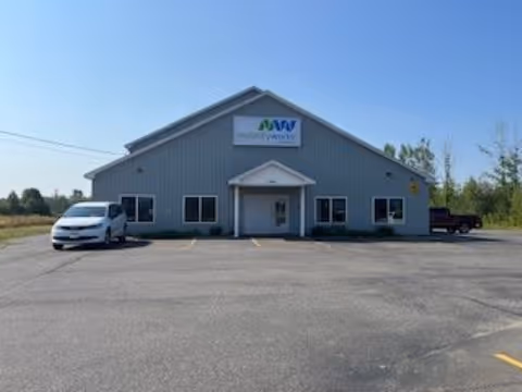 Front view of a MobilityWorks facility with a sign, parking lot, and clear blue sky.