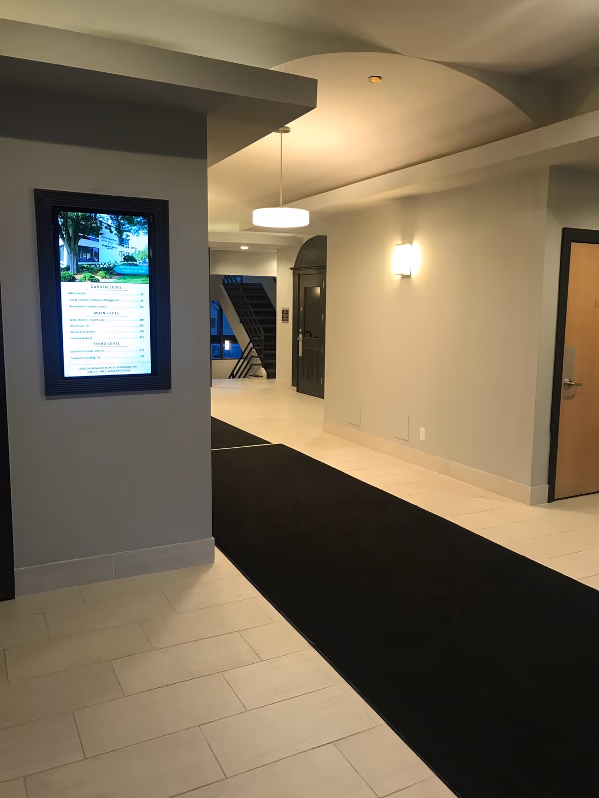 Interior hallway of a senior living facility with a black carpet runner and framed directory