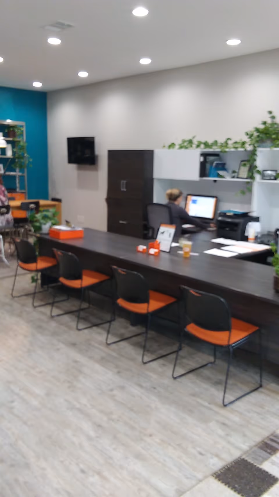 Reception area inside Right at Home facility with dark counter, orange chairs, and staff at computer.