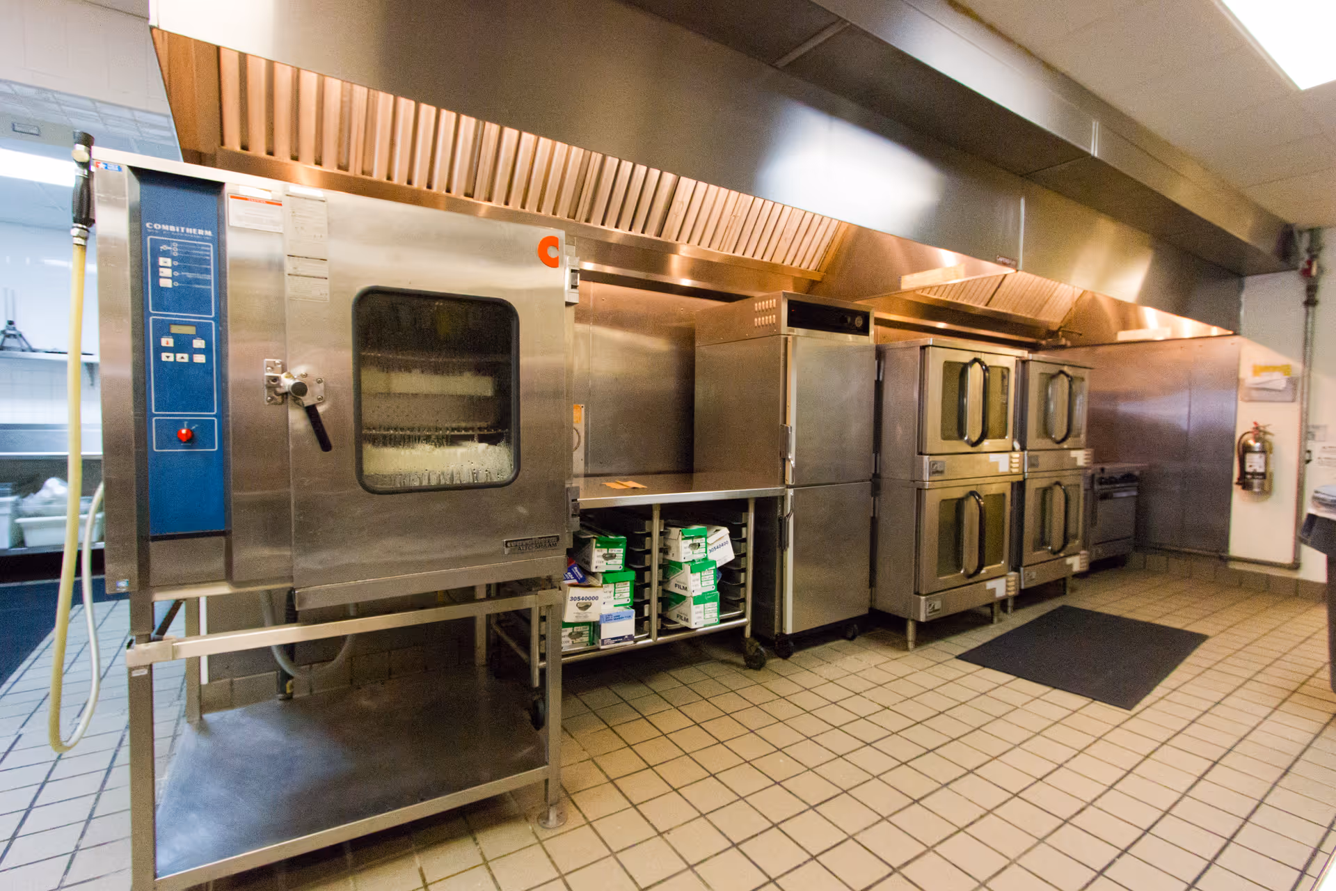 Industrial stainless-steel kitchen with commercial ovens and tiled floor.