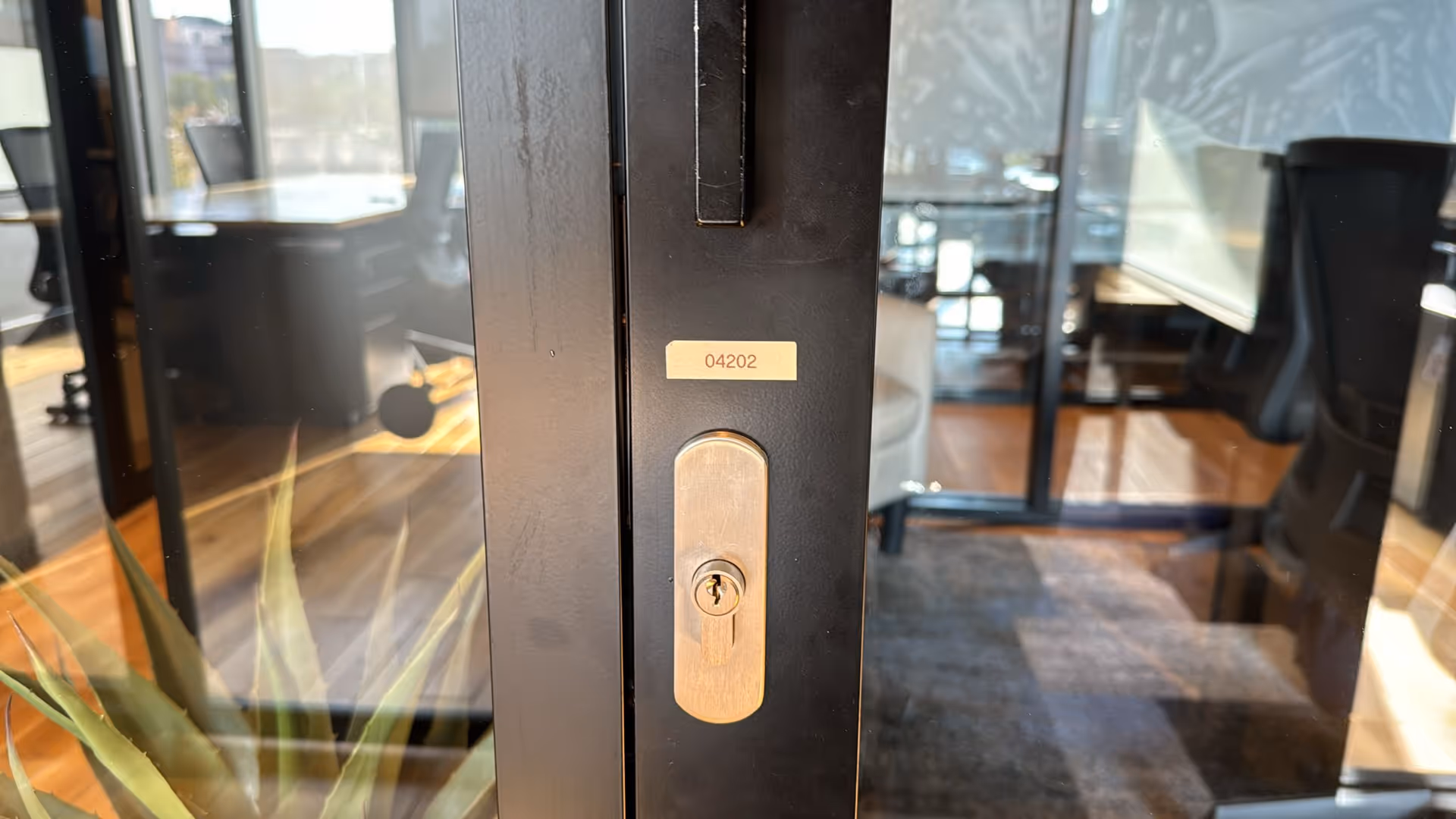 Close-up of a glass door with a metal handle, revealing an office interior.