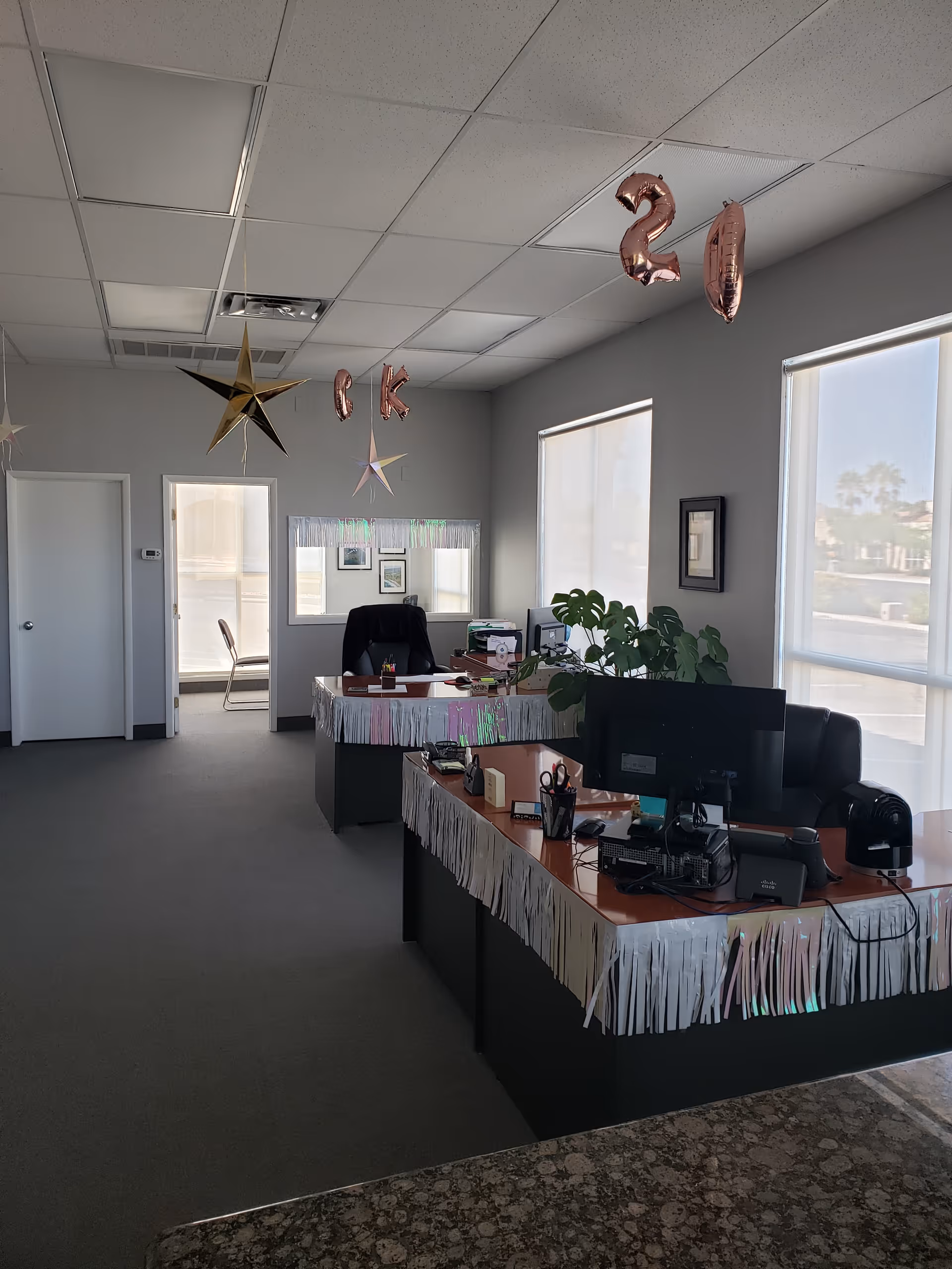 Lobby reception area in a senior care facility with two desks, festive streamers, balloons, and plants.