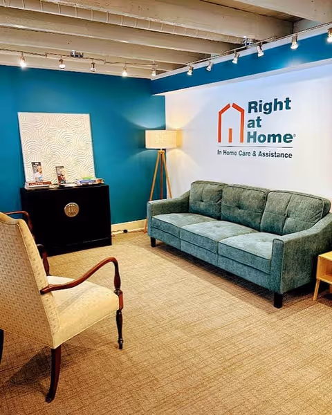 Interior lounge area with teal wall, sofa, chair, and Right at Home sign.