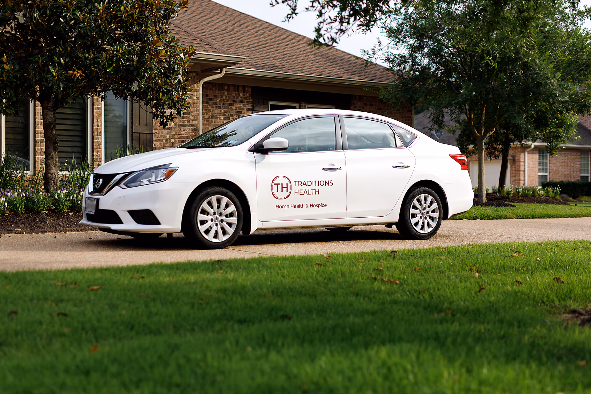 White car with Traditions Health logo parked in front of a brick building.