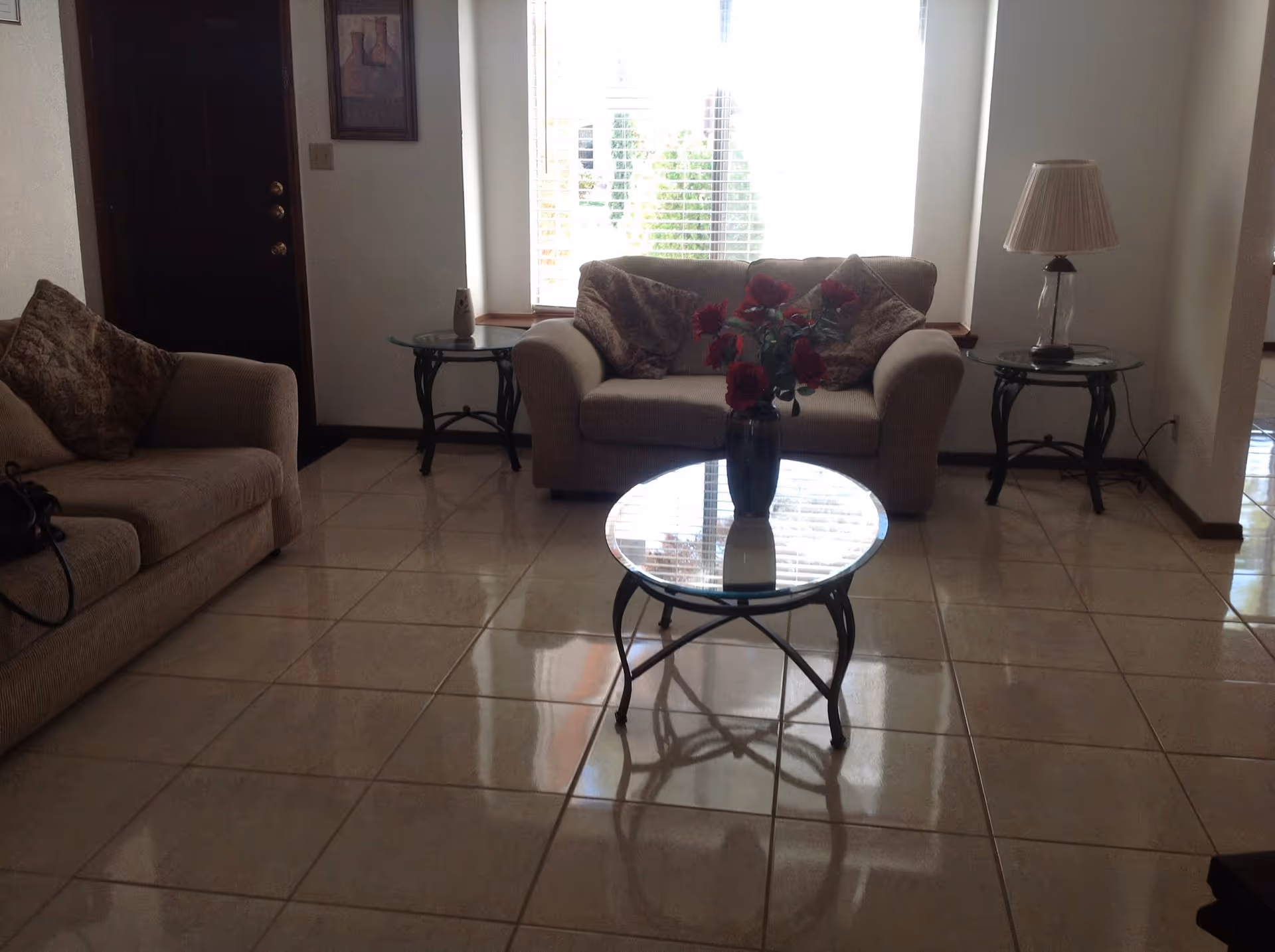 Bright living room with beige sofas, glass coffee table, and red flowers.