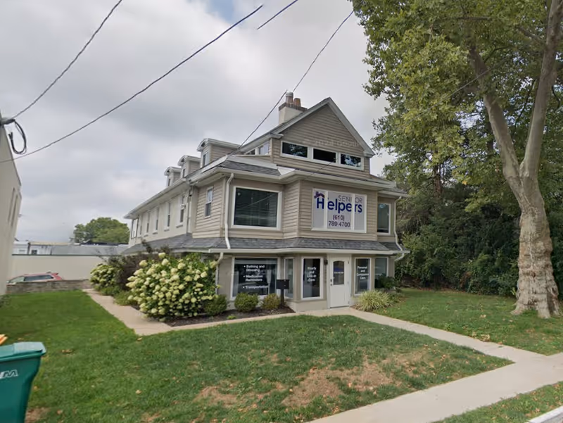 Two-story Senior Helpers facility with a front sign, windows, and surrounding lawn.