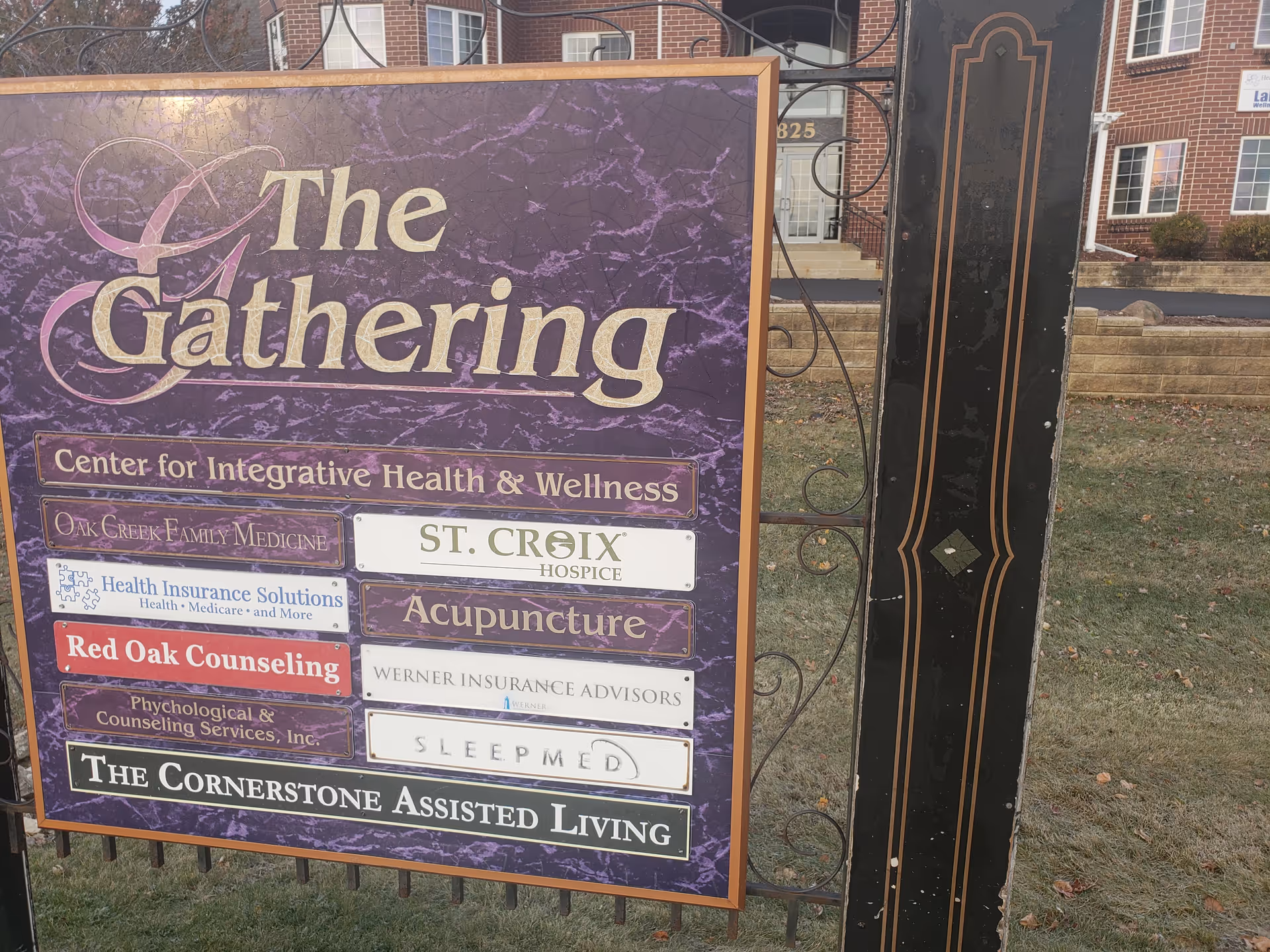 A large purple signboard for The Gathering and St. Croix Hospice outside a brick building.