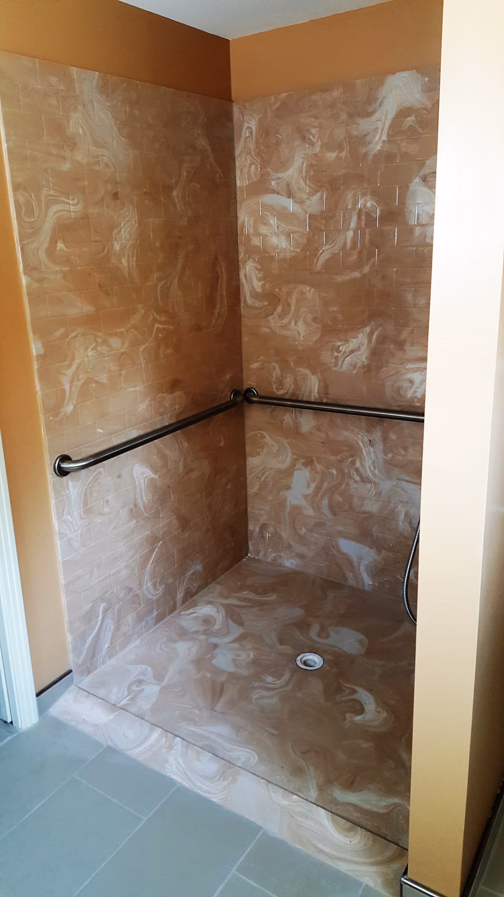 An accessible marble-pattern shower stall with brown tiles, grab bars, and a handheld shower.