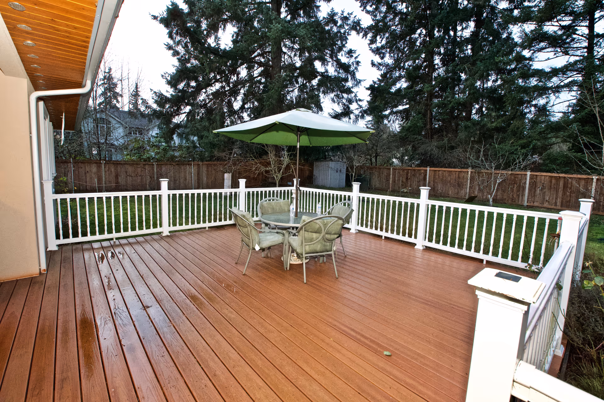 An outdoor wooden deck with a table, chairs, and a green umbrella.