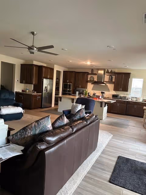 Open-concept living area with brown leather sofa, dark wood cabinets, and a kitchen island.