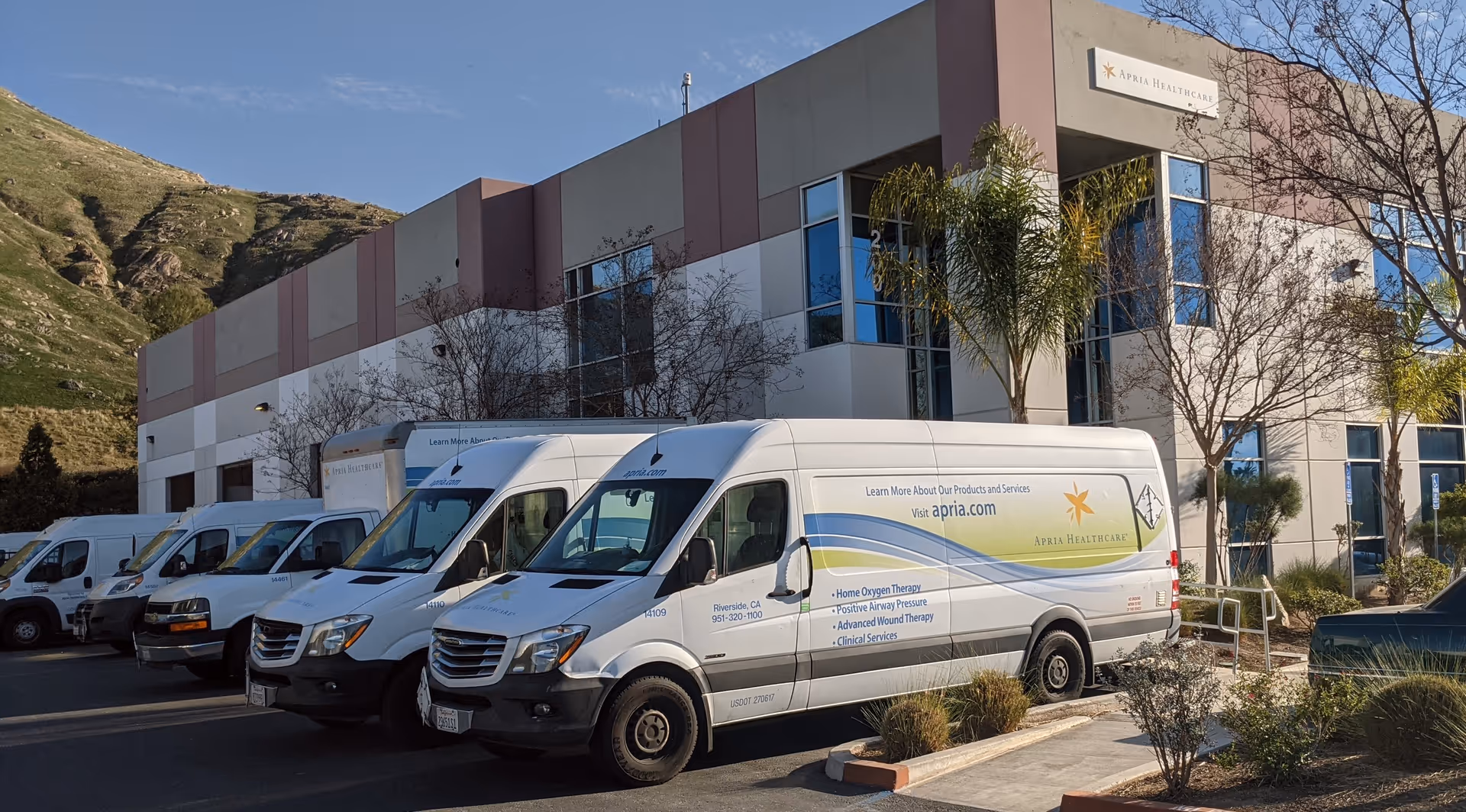 Exterior view of Apria Healthcare facility with white delivery vans parked outside.