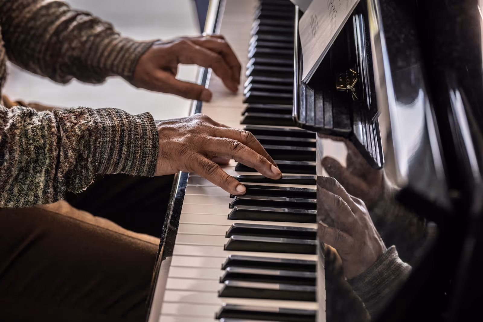 Close-up of senior hands playing a piano keyboard with reflections on its surface.