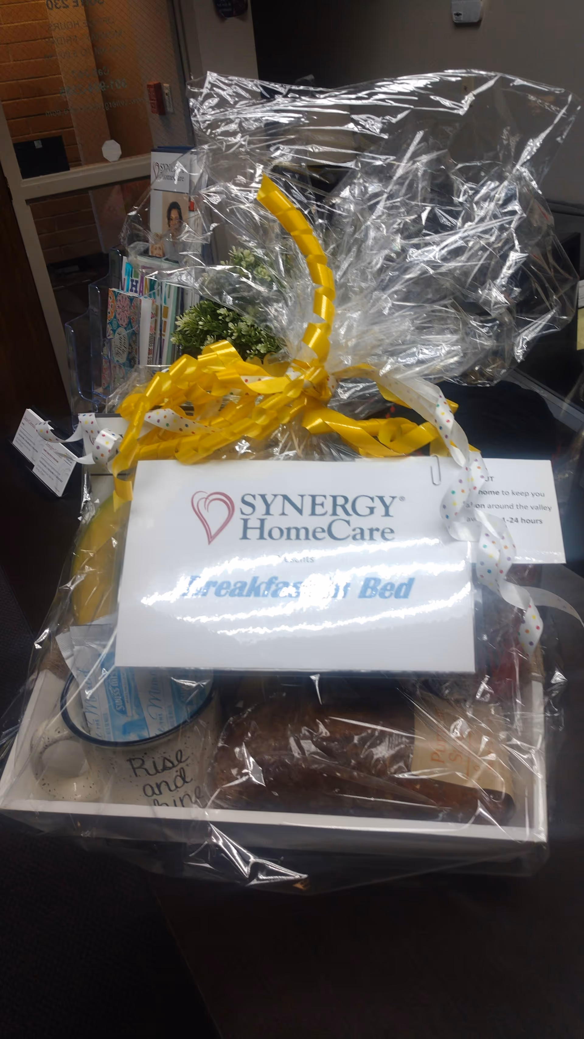 Gift basket wrapped in plastic with yellow ribbons and a Synergy HomeCare sign