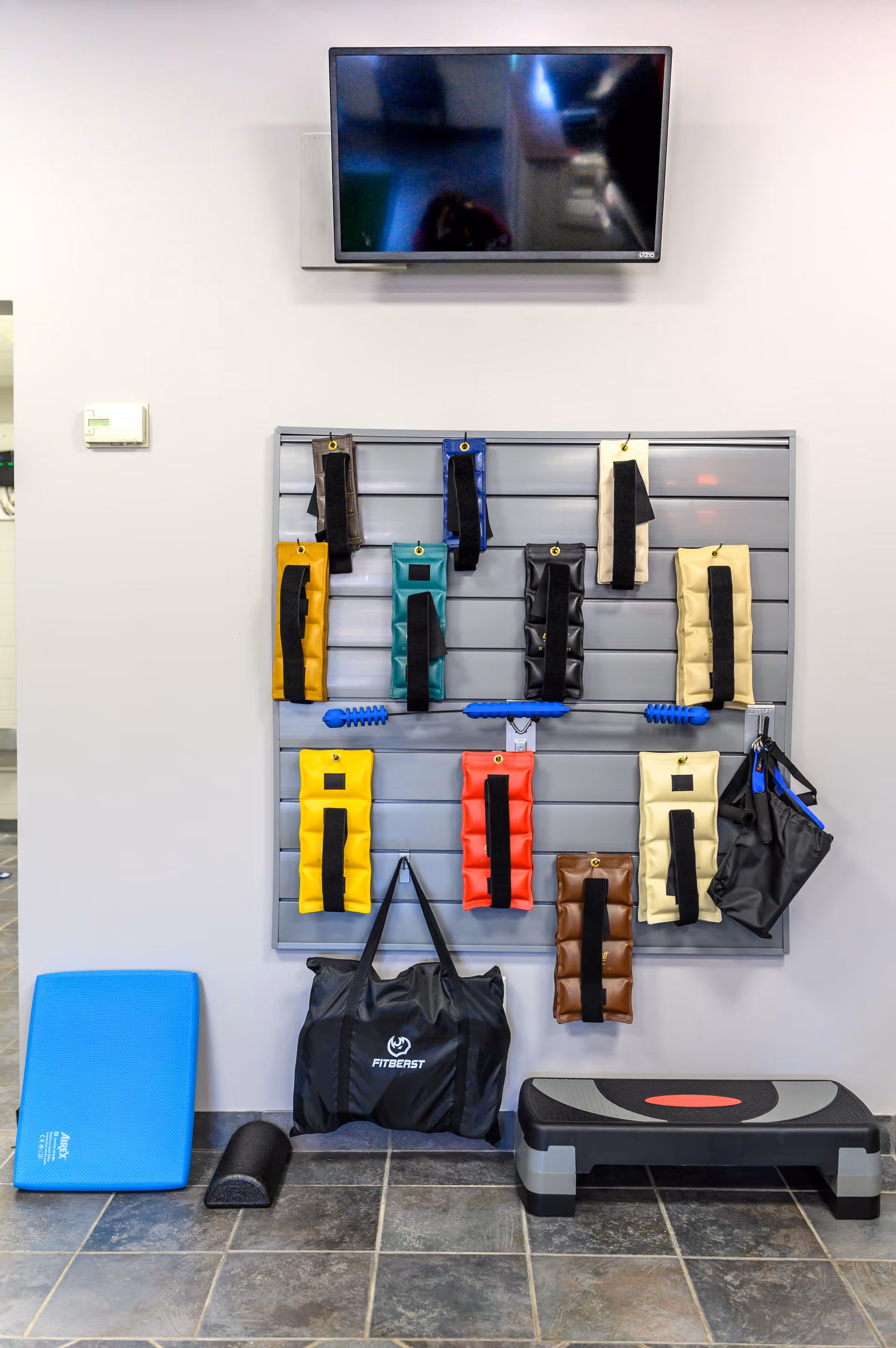 TV above a wall-mounted array of colorful resistance bands and fitness gear in an interior gym.