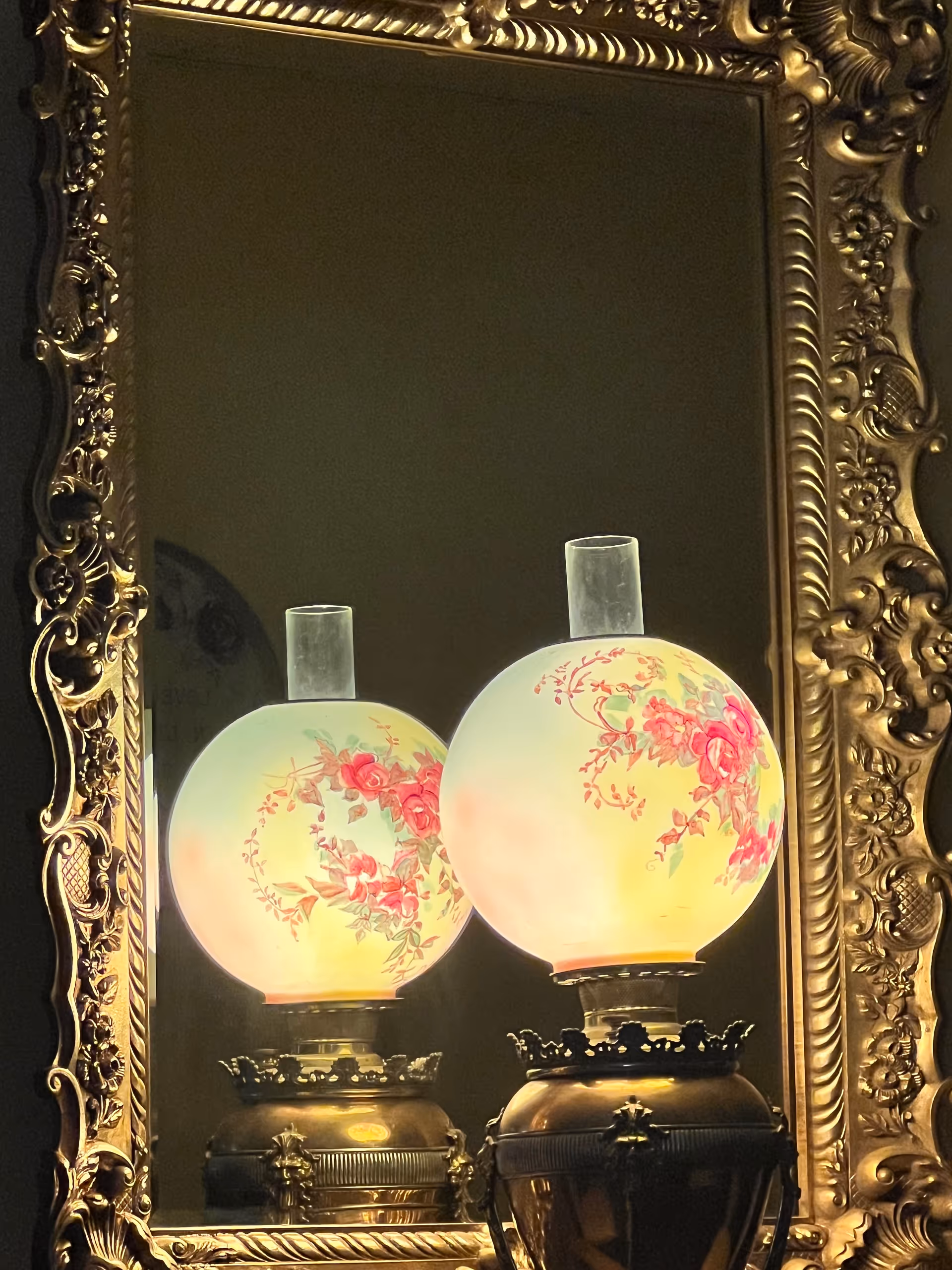 Ornate gold-framed mirror reflecting two glowing floral-patterned lamps.