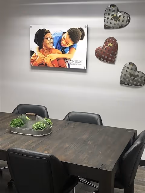 A dining table with chairs in a SYNERGY HomeCare dining area; wall art is visible.