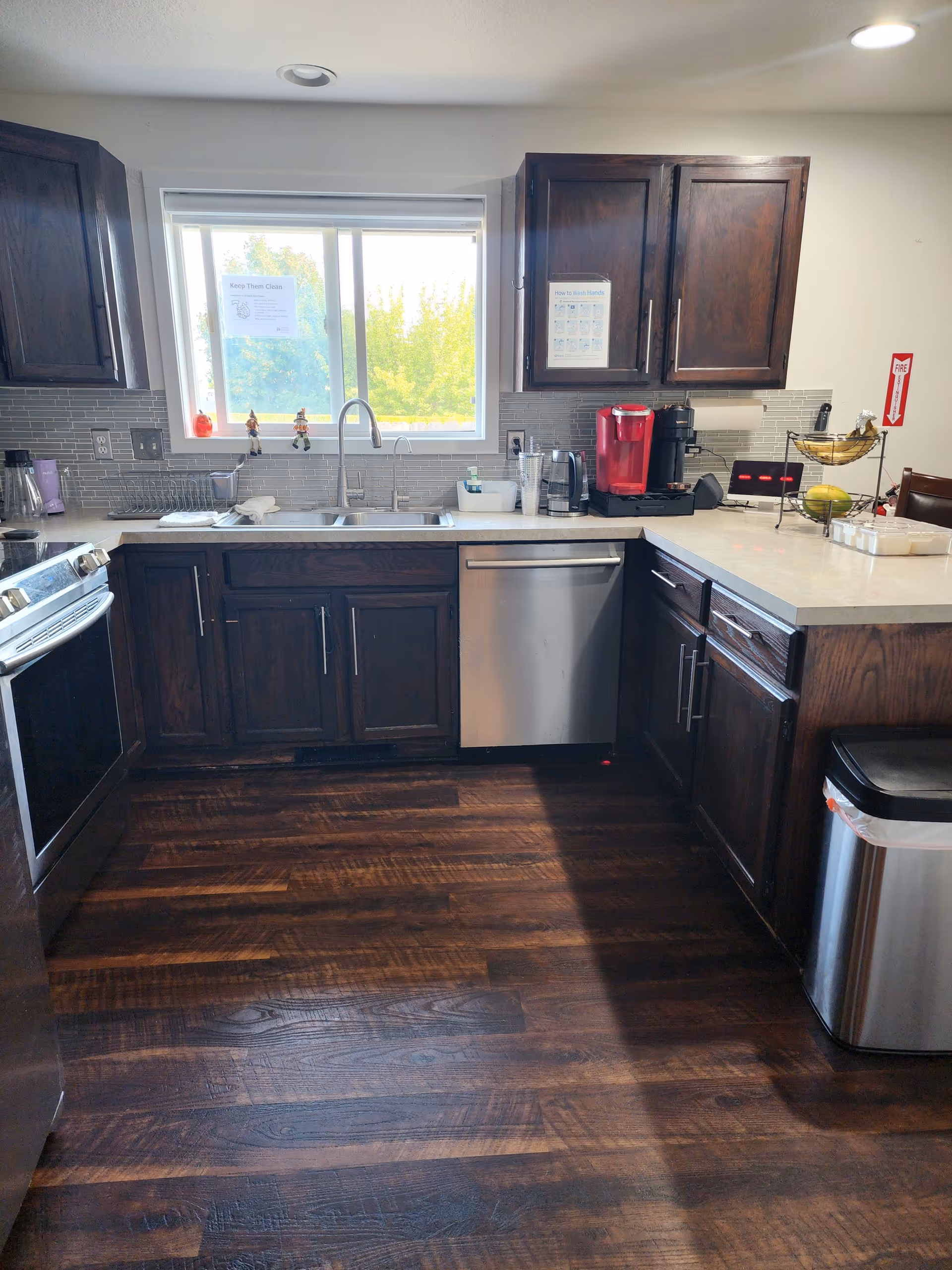 Compact kitchen with dark wood cabinets, stainless appliances, and a window behind the sink.