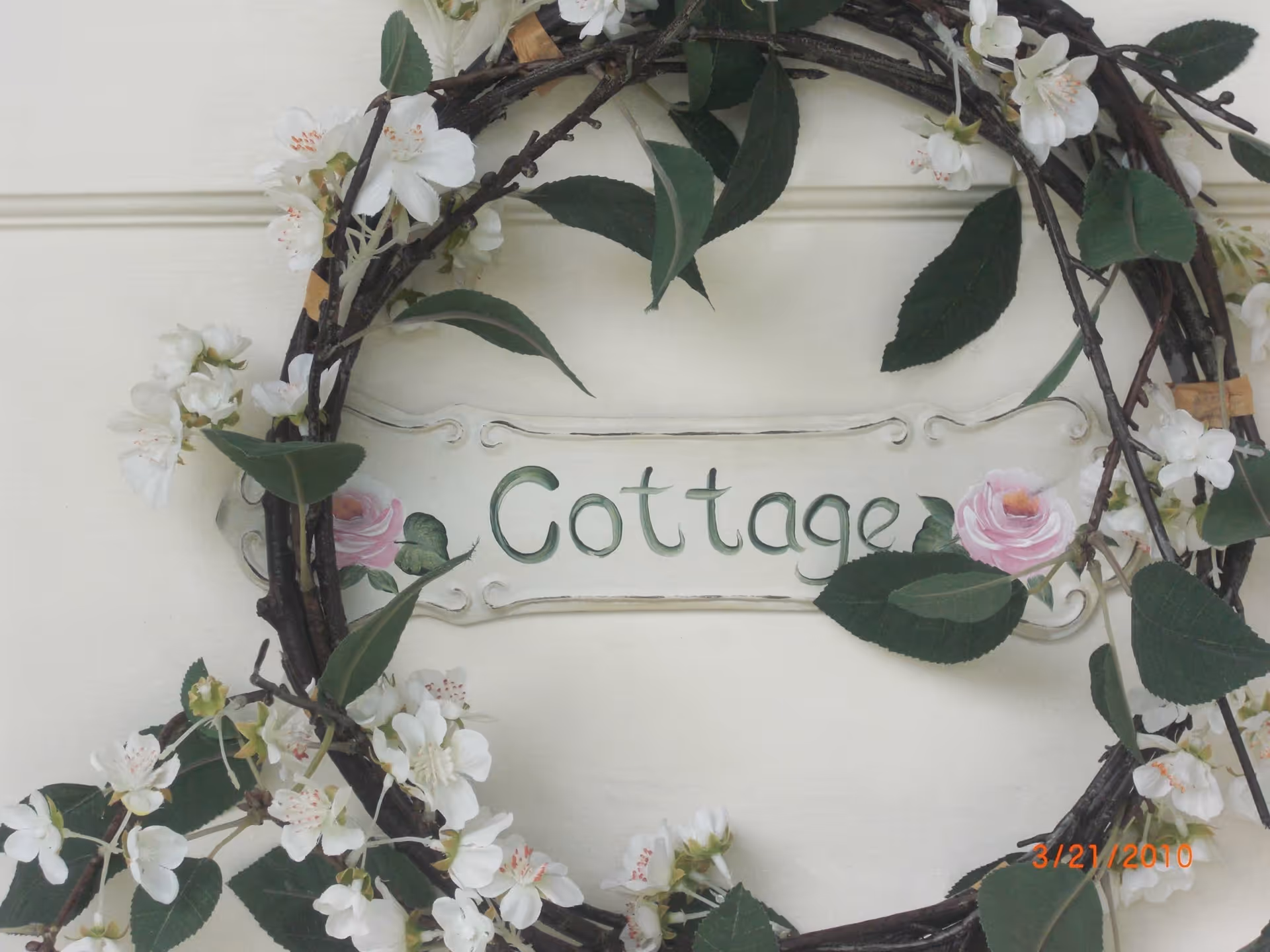 White exterior wall with floral wreath framing a Cottage sign.