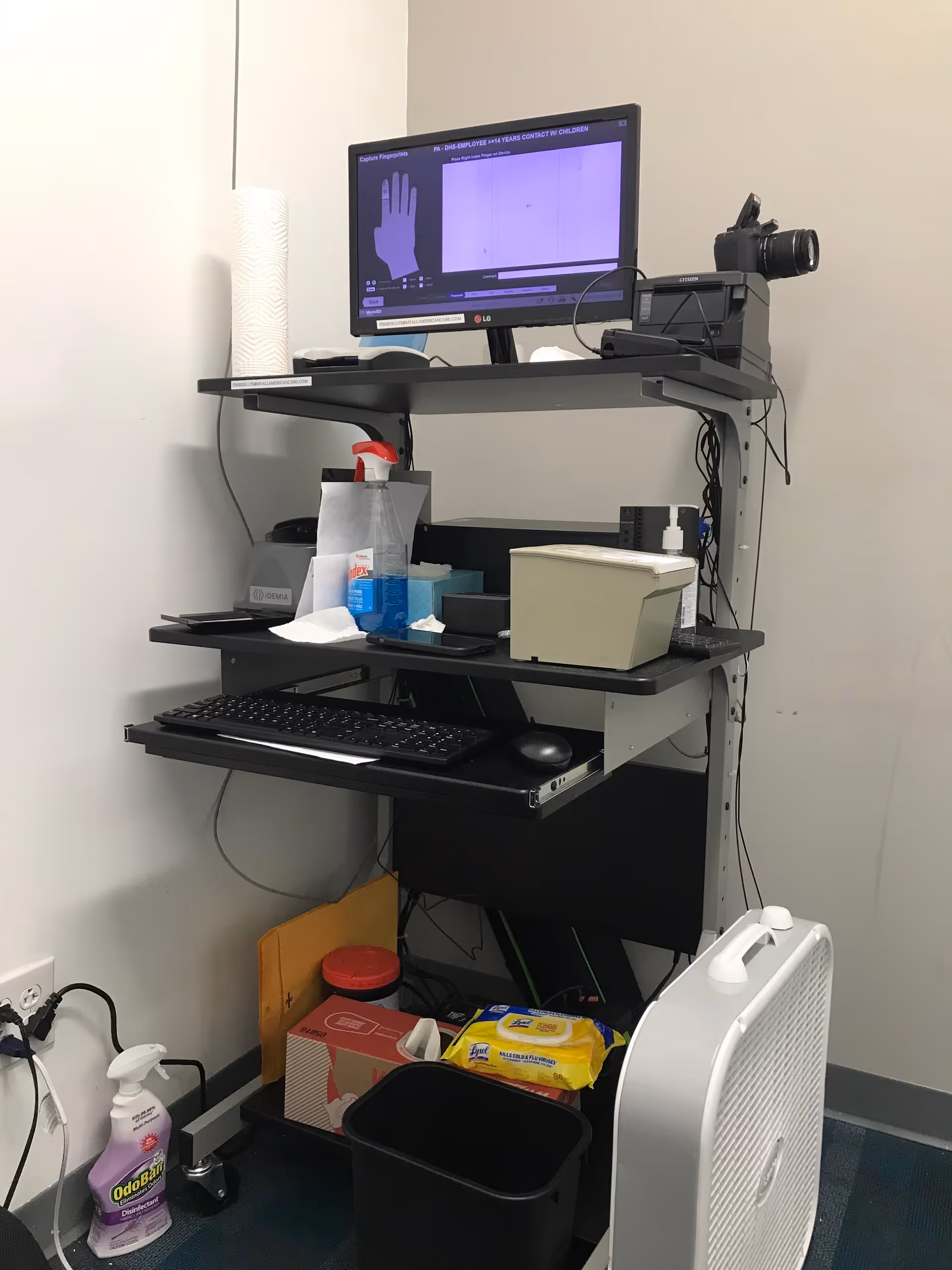 Compact interior workstation with computer monitor, keyboard, printer, and cleaning supplies.