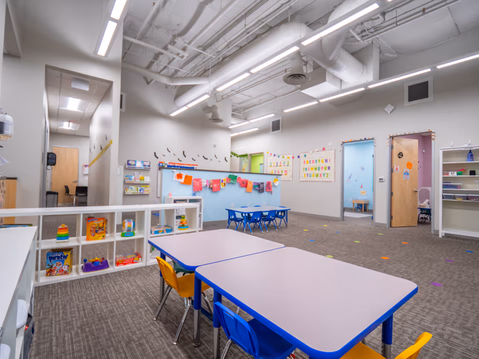 Bright, spacious interior activity room with colorful tables, chairs, and toy shelves.