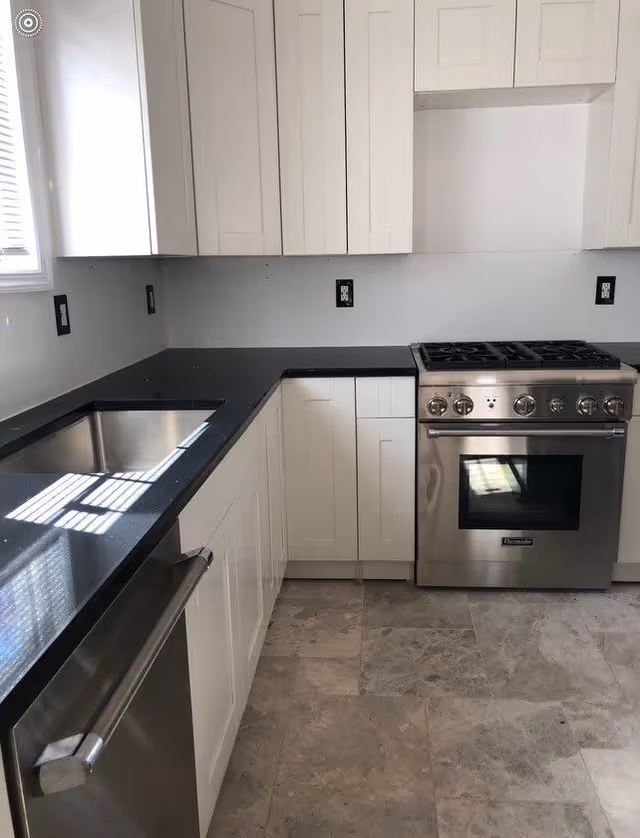 Bright modern kitchen with white cabinets, black countertops, and stainless steel appliances.