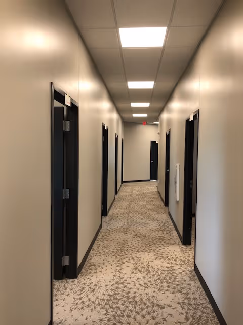 A long, well-lit beige hallway in a senior living facility with multiple doors.