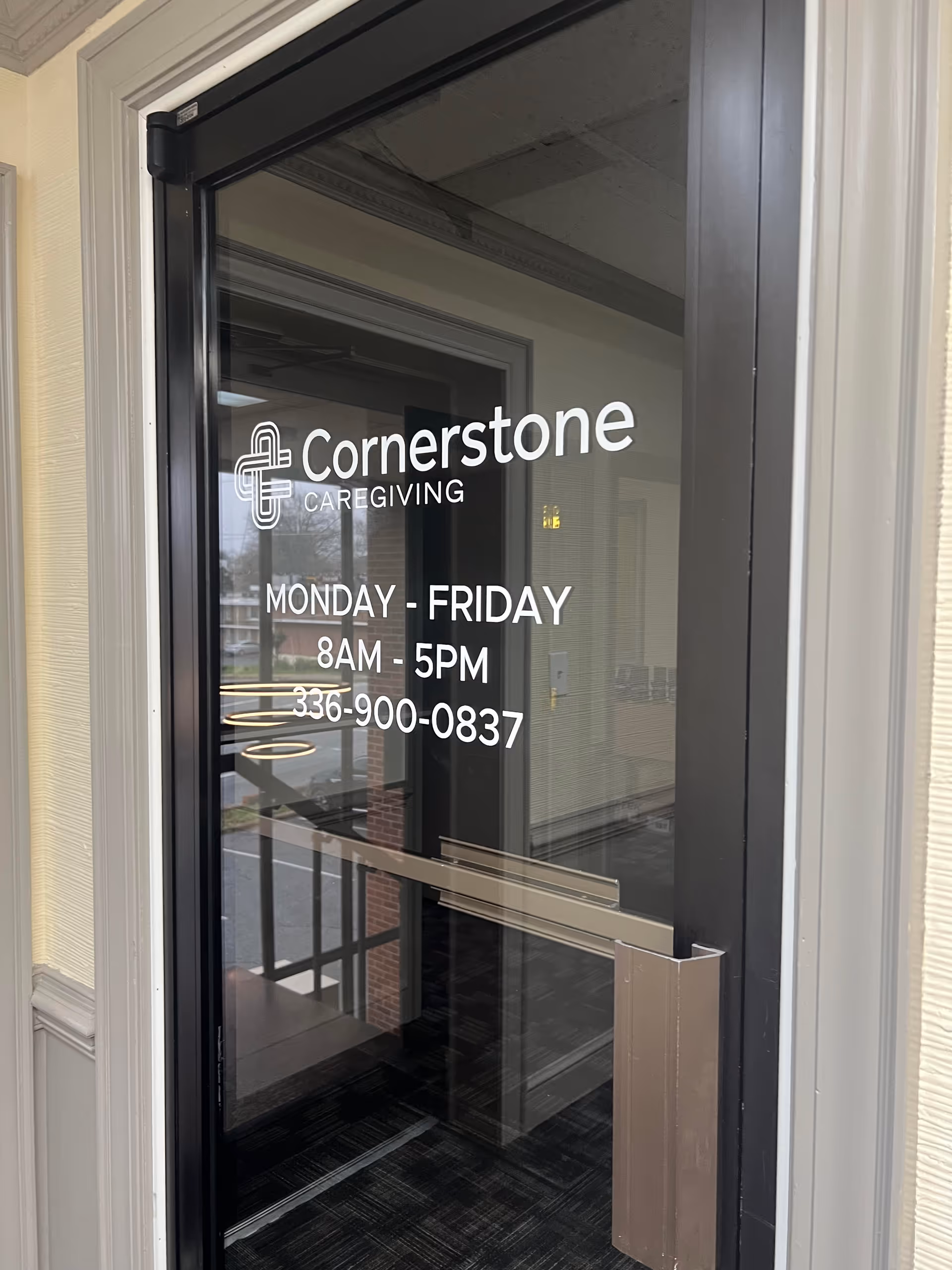 Glass door entry displaying Cornerstone Caregiving logo and hours, outside facility entrance.