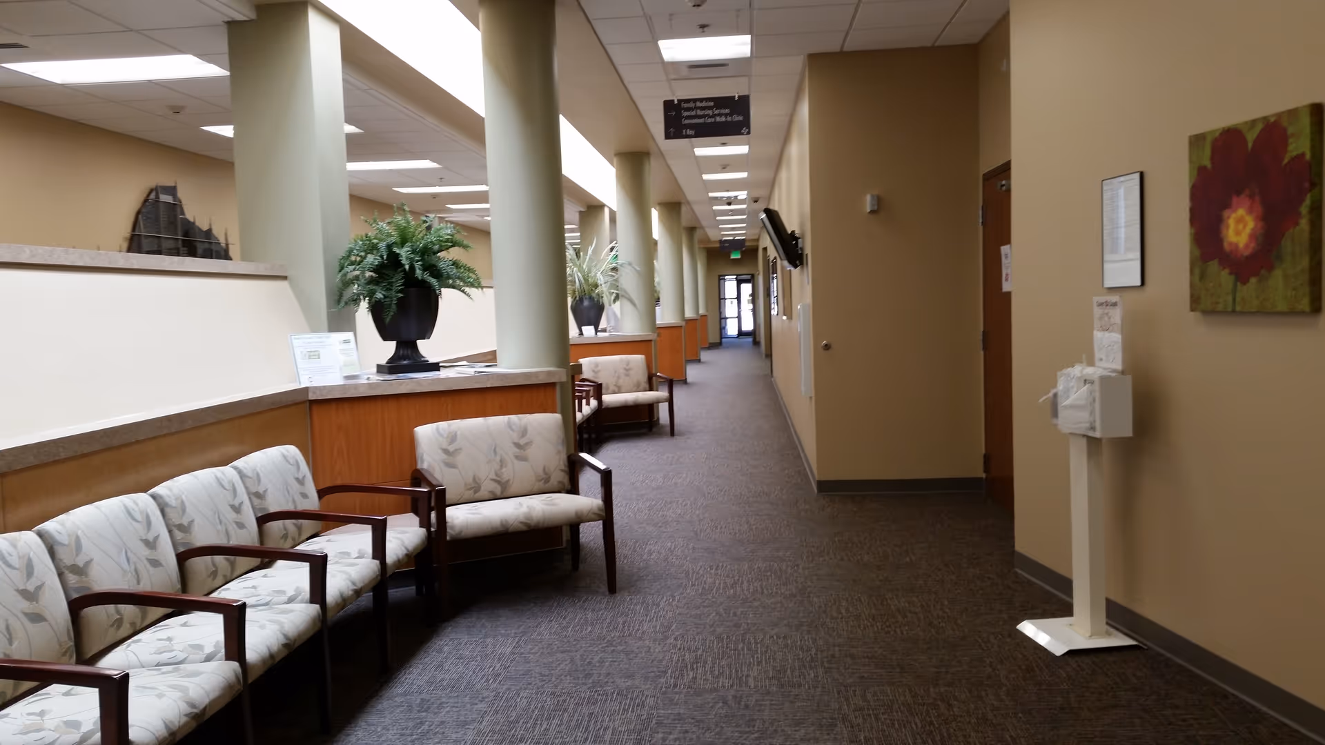 Interior hallway of a senior living facility with chairs, plants, and signage.