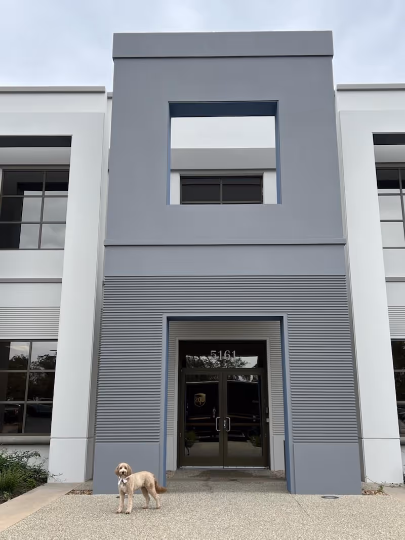 Modern facility entrance with a small dog standing on the front sidewalk.