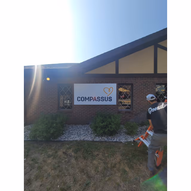 Exterior brick Compassus building with sign and a person near the entrance.