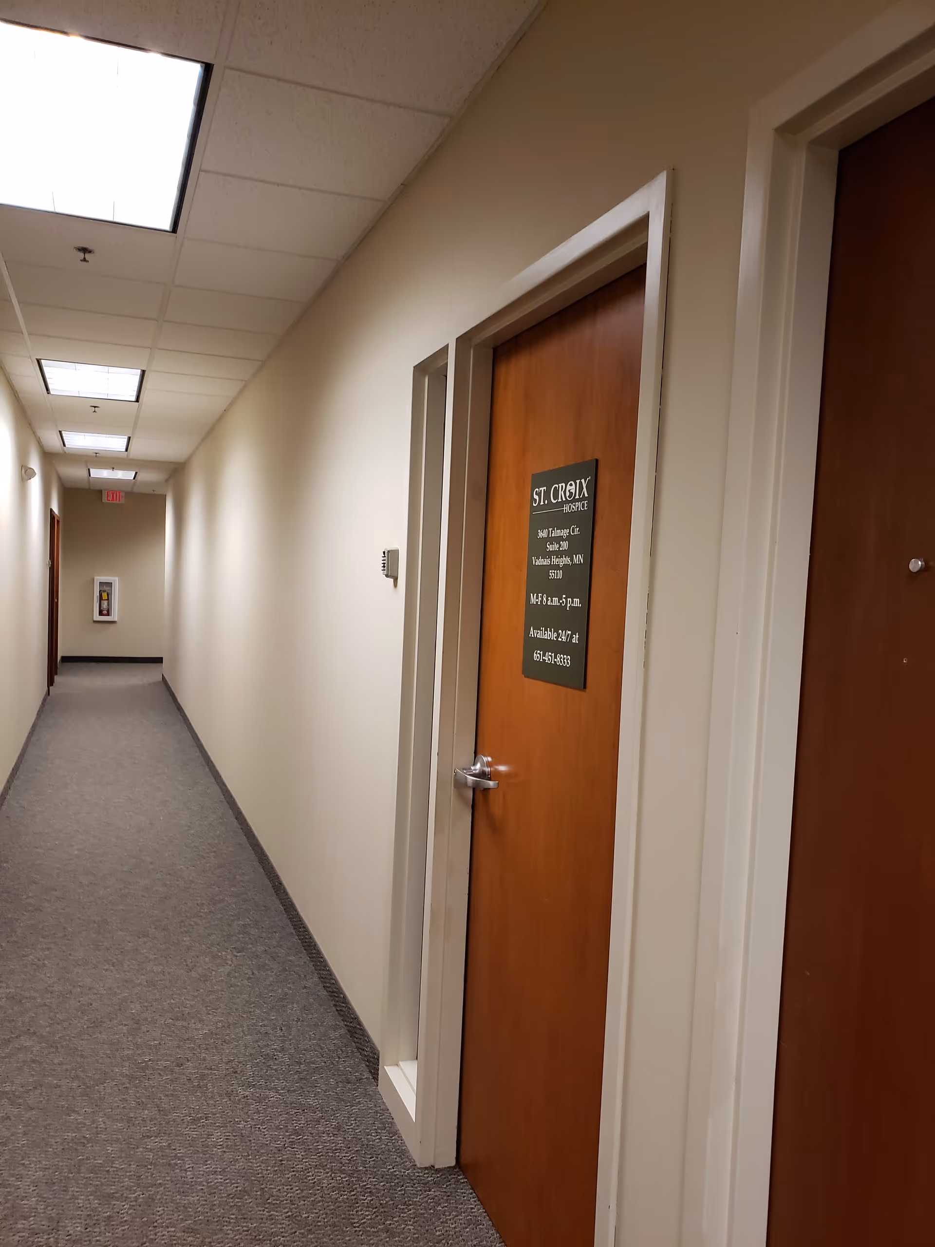 Long beige hallway in a St. Croix Hospice facility with wooden doors and signs