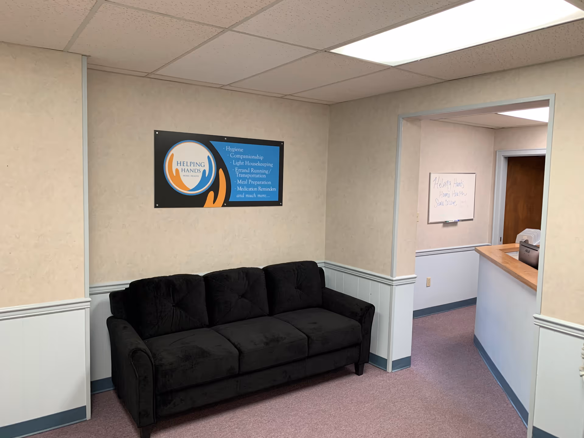 A black sofa sits in a beige-walled lounge area near a reception doorway.