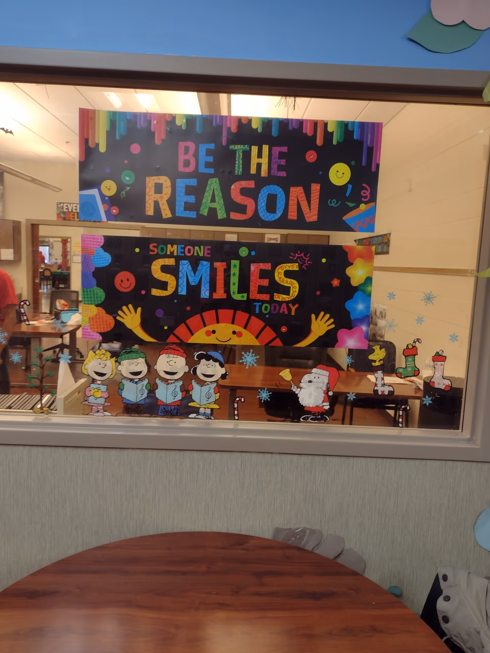 Window into a decorated activity room with colorful banners, cartoon cutouts, and holiday figures.