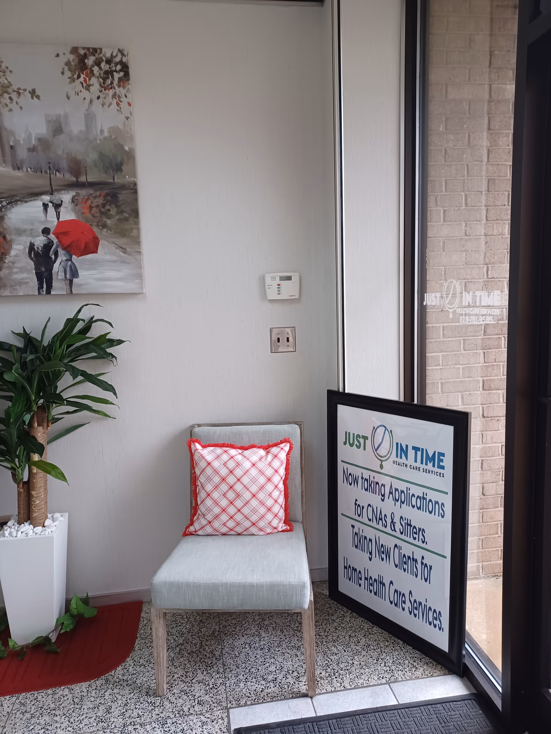 Indoor lobby area with a chair, plant, wall art, and framed sign near entrance.