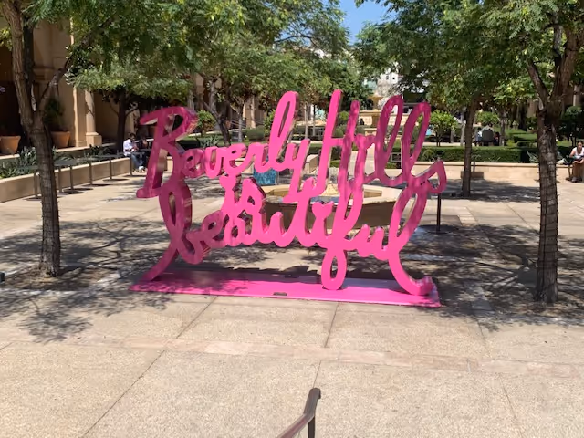 Outdoor plaza with a bright pink Beverly Hills Beautiful sculpture among trees.