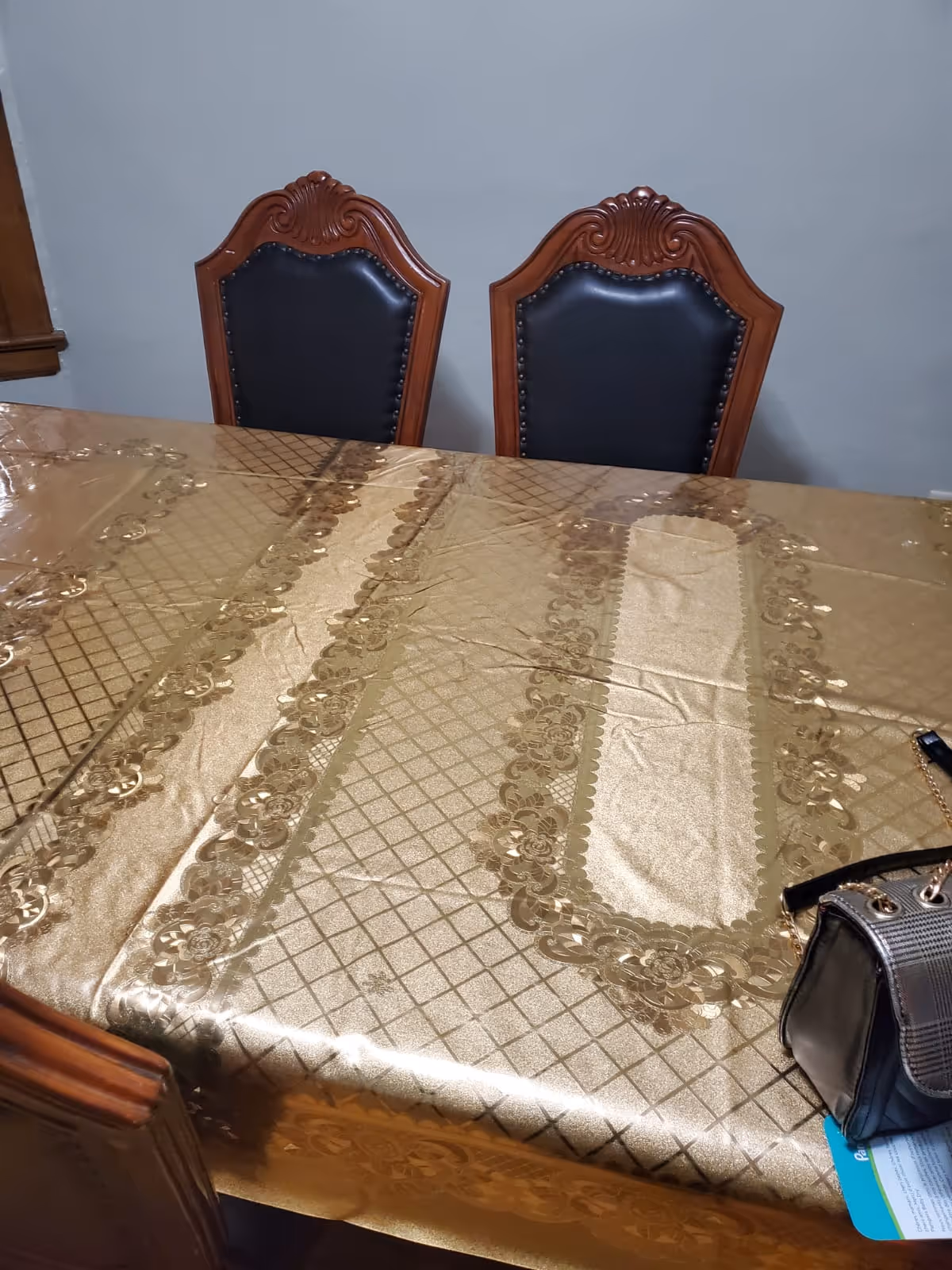 A gold-patterned dining table with two ornate wooden chairs in a formal dining room.